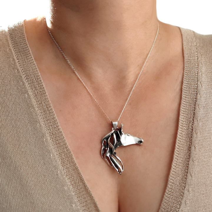 Silver horse pendant necklace on a woman wearing a beige top