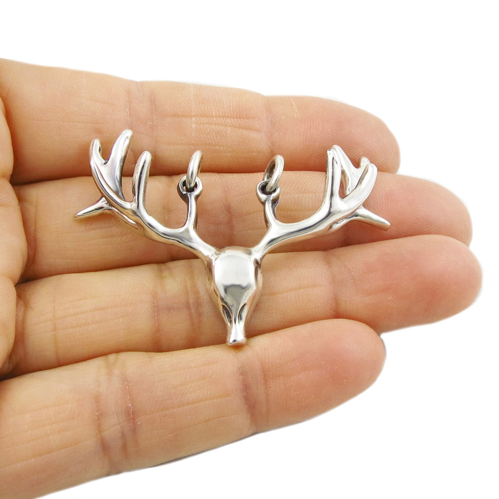 Large silver reindeer pendant jewellery held in a person's hand on a white background. 