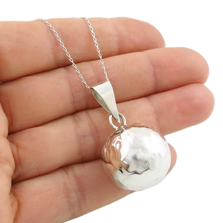 A Mexican sterling 925 silver large pendant necklace with a hammered, textured spherical ball bola chime, shown resting on a person's hand against a white background.