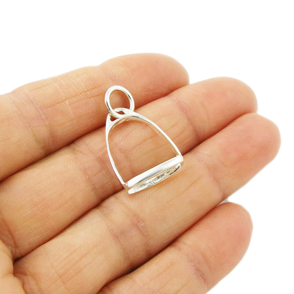 Silver horse stirrup pendant held between fingers on a white background