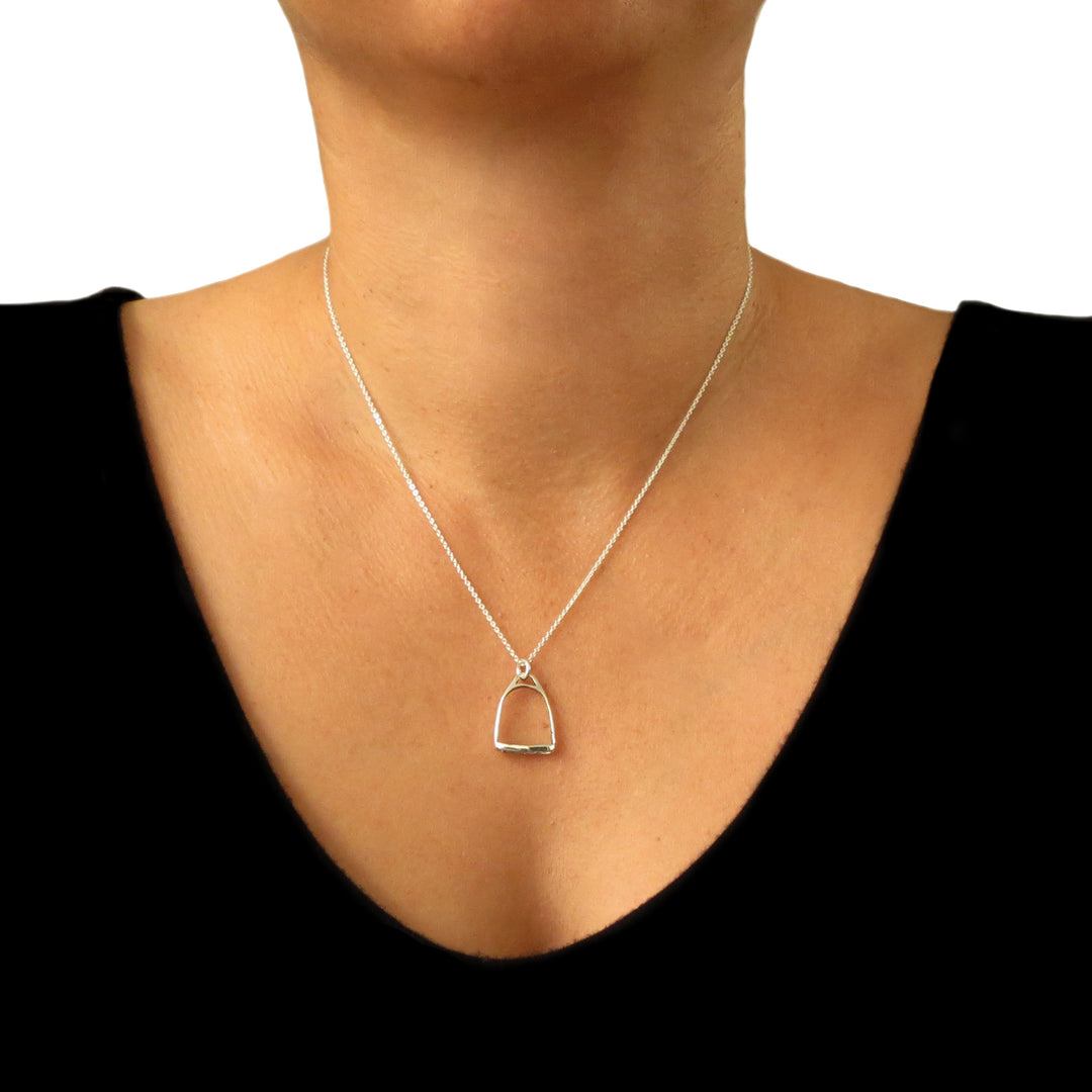 Silver necklace with a horse sstirrup pendant on a person wearing a black top.