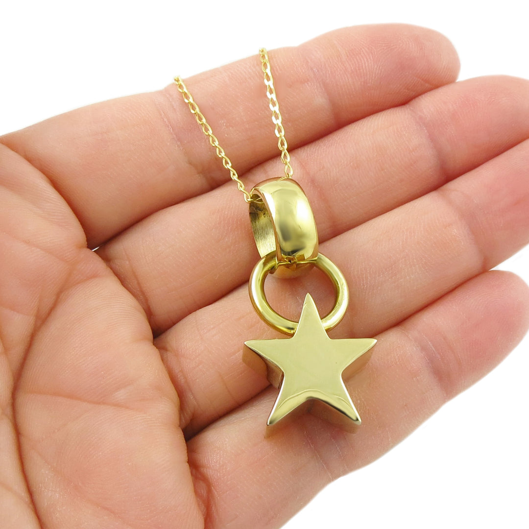 Gold necklace with a star pendant held in a hand against a white background