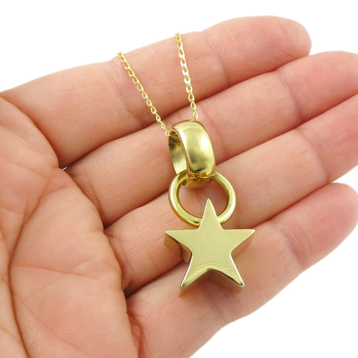 Gold necklace with a star pendant held in a hand against a white background