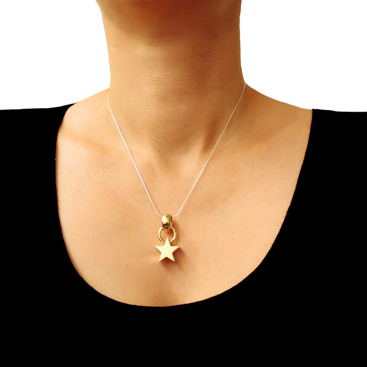 Gold star pendant necklace on a person wearing a black top against a white background
