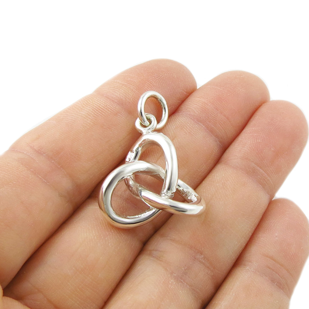 Silver eternity love knot pendant held in a person's hand on a white background. 