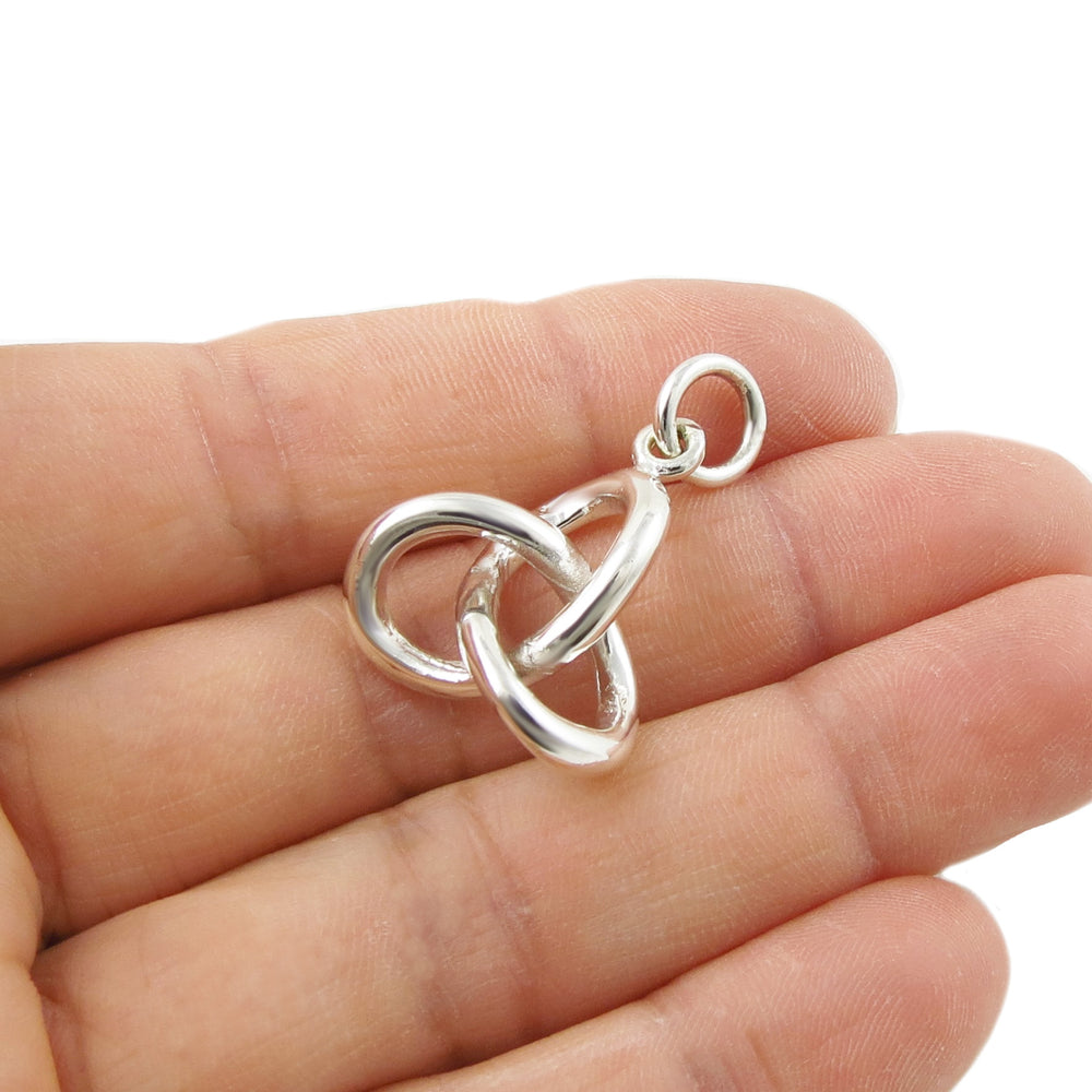 Silver love knot pendant held between fingers on a white background