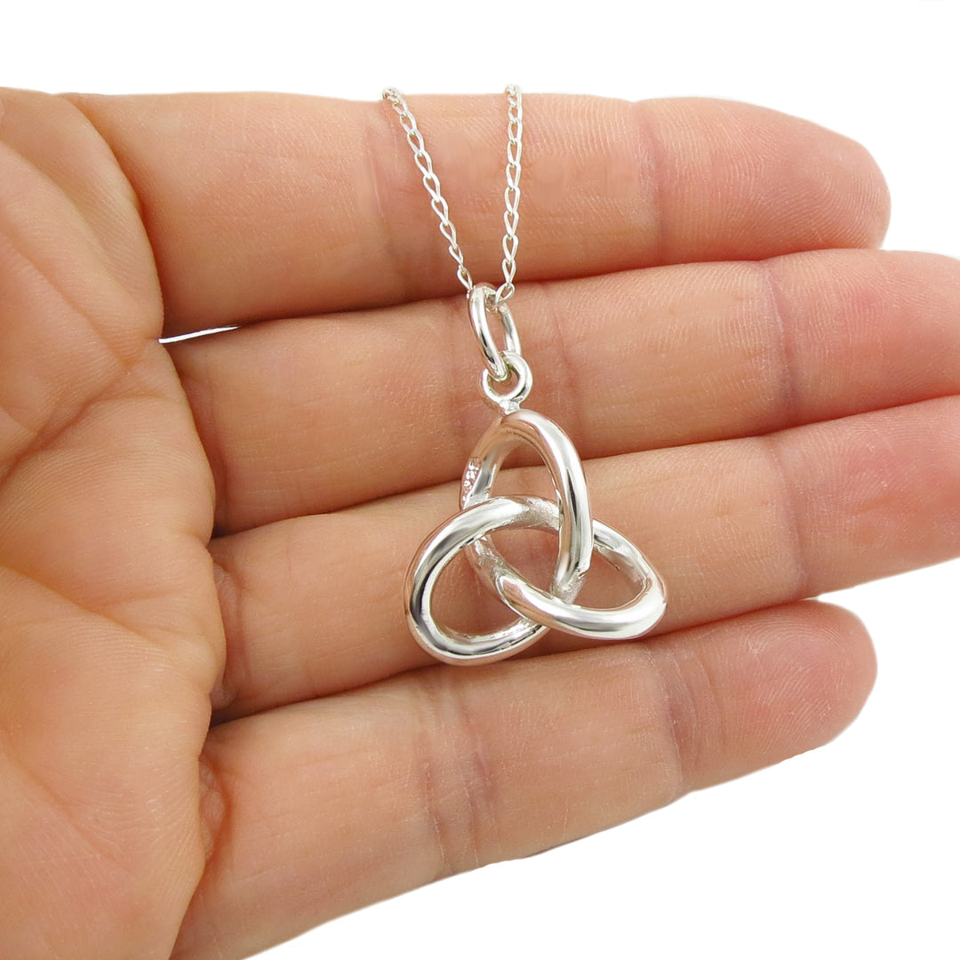 An infinity knot pendant and chain necklace in silver held in a person's hand. 