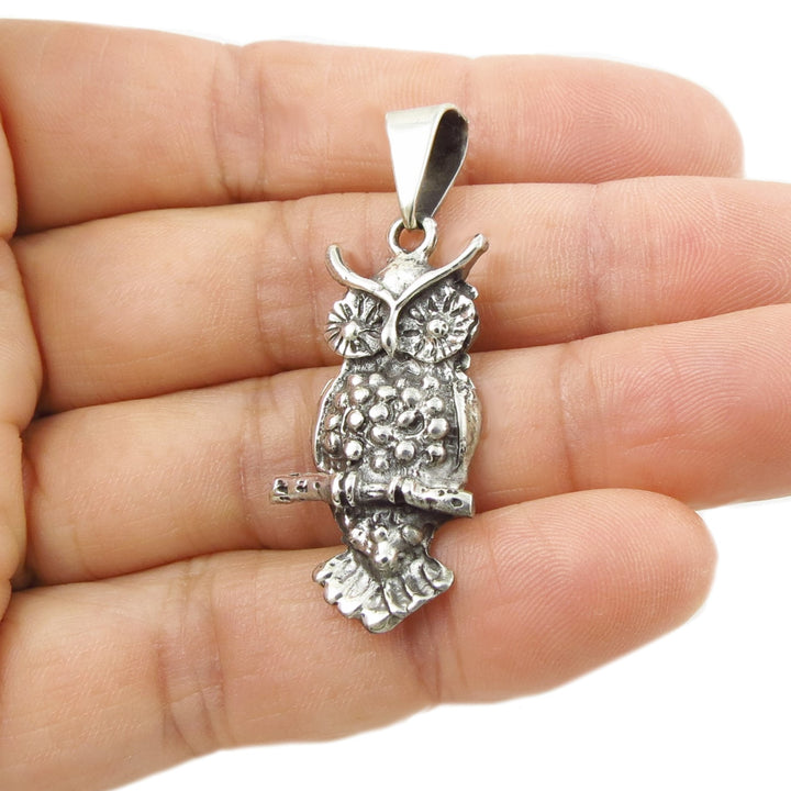 Silver owl pendant held between fingers against a white background