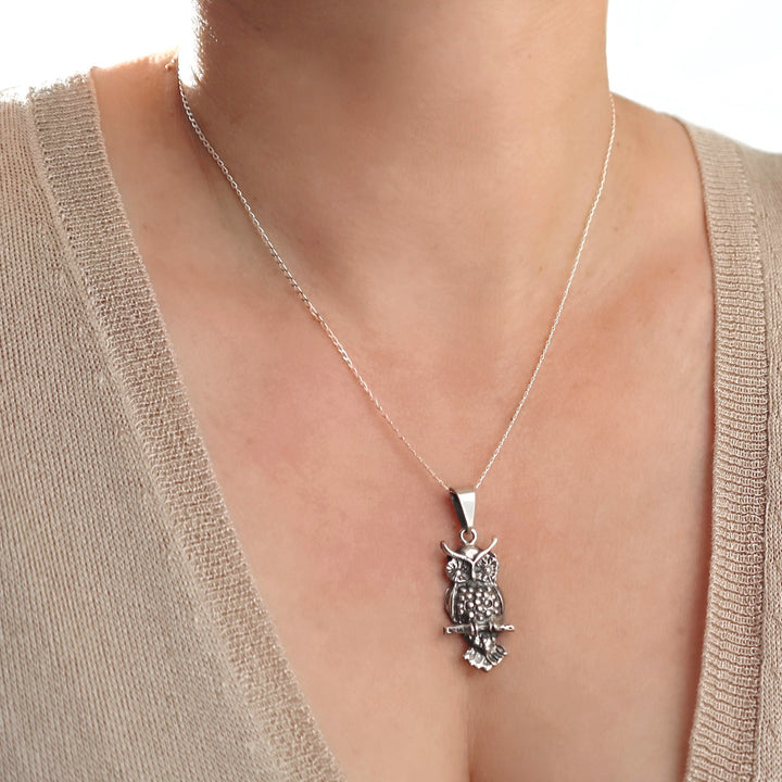 Silver owl pendant necklace on a woman wearing a beige top.