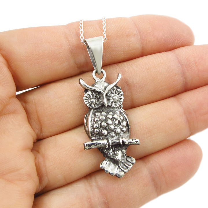 Silver owl pendant on a chain held in a hand against a white background