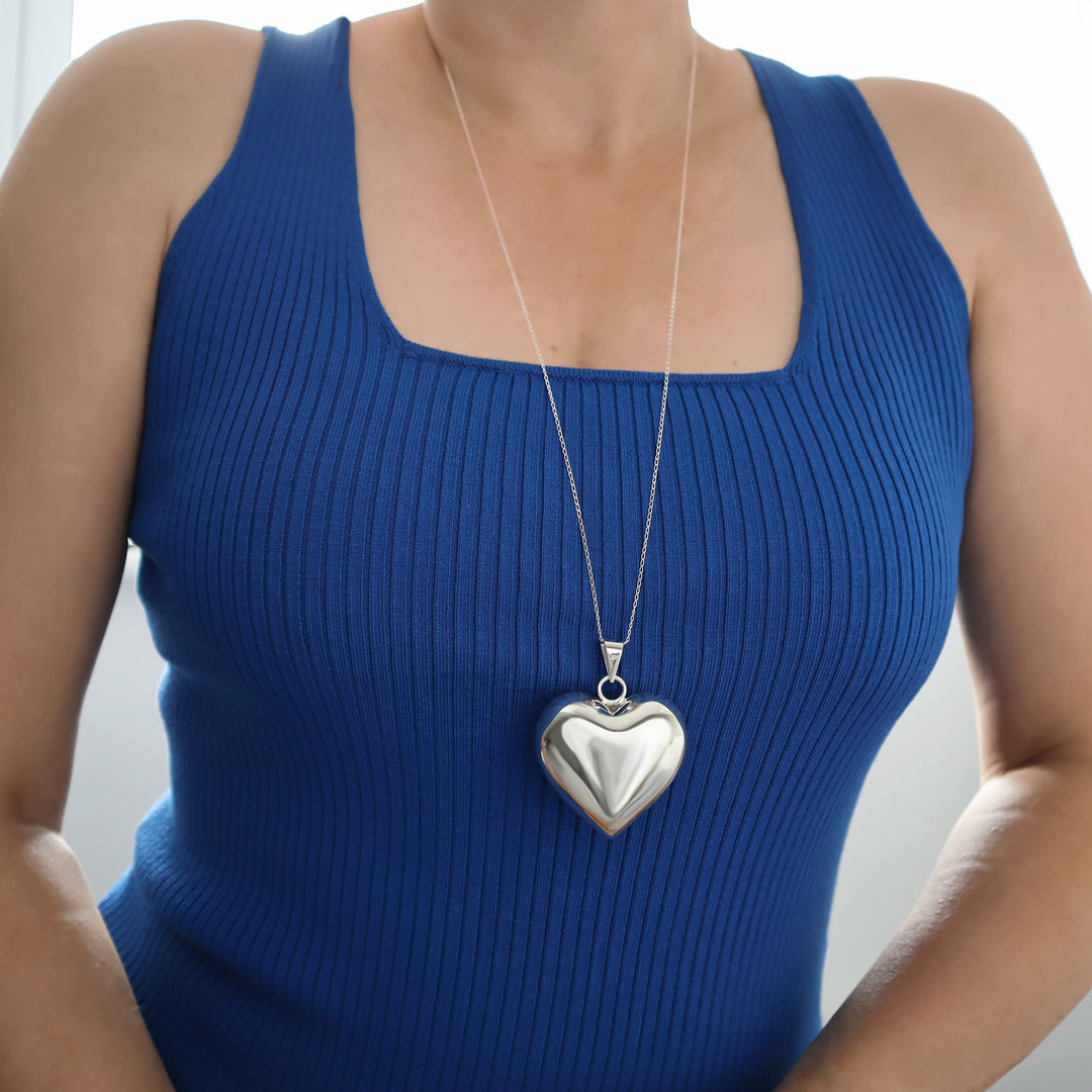 A woman wearing a blue tank top with a silver puffed heart-shaped pendant necklace.