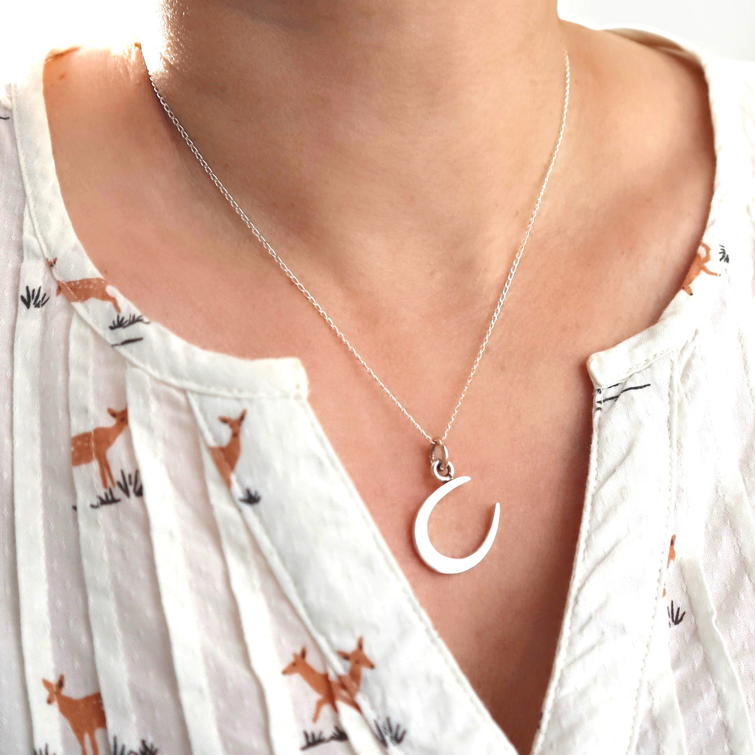 A woman in a white blouse wearing a silver horseshoe necklace.