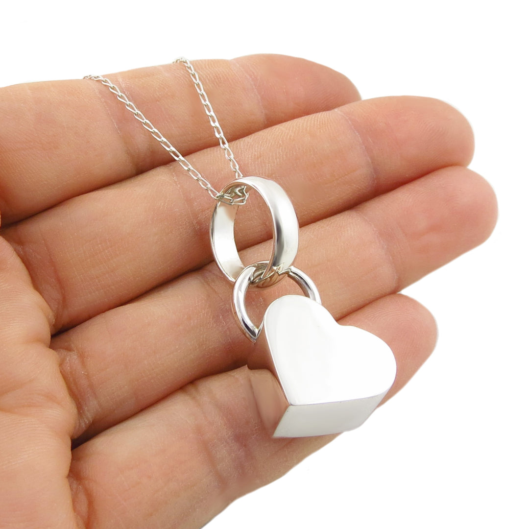 A UK hallmarked 925 sterling silver pendant necklace with a puffed love heart-shaped tag and a small ring, held in a person's hand against a white background.