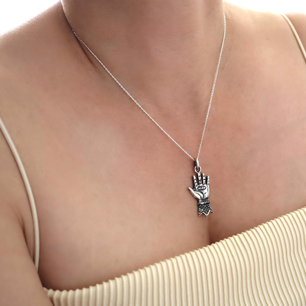 Silver necklace with a hand of hamsa  pendant on a person wearing a beige top.
