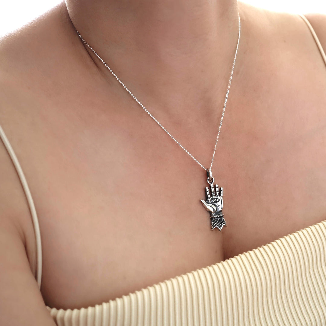 Silver necklace with a hand of hamsa  pendant on a person wearing a beige top.