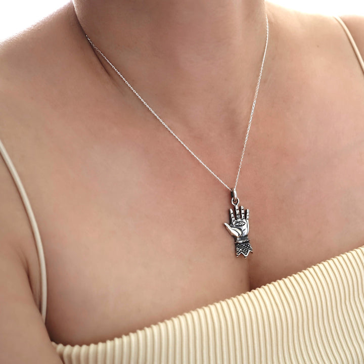 Silver necklace with a hand of hamsa  pendant on a person wearing a beige top.