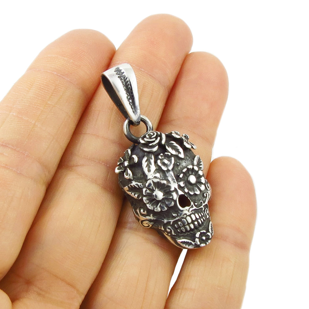 A sterling silver pendant in the shape of a day of the dead skull with floral patterns held in a person's hand.