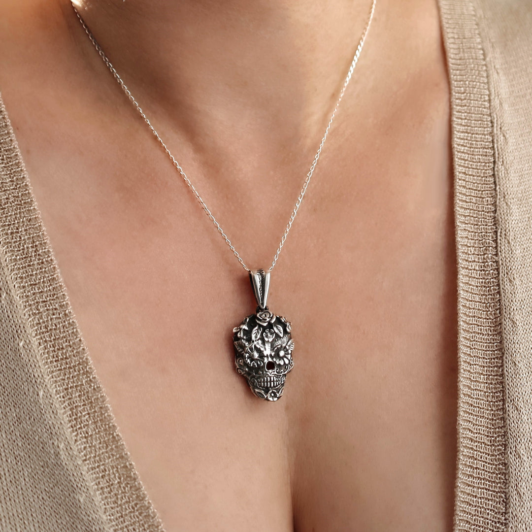A close-up of a woman wearing a Mexican 925 sterling silver pendant necklace with an ornate day of the dead sugar skull design, styled with a beige knit cardigan.