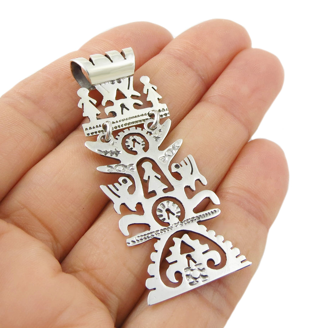 Silver pendant with intricate tree of life designs held in a hand against a white background