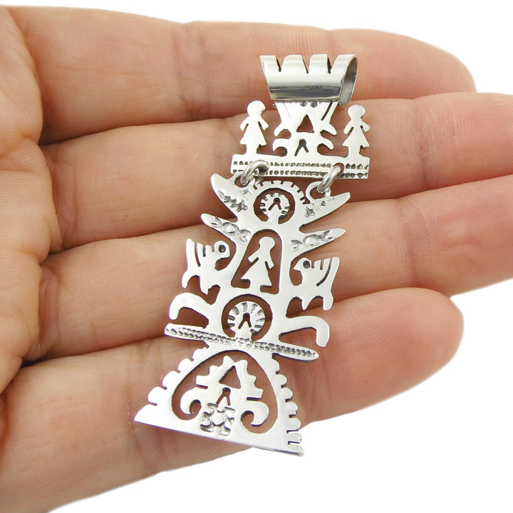 Silver pendant with intricate tree of life designs held in a hand against a white background