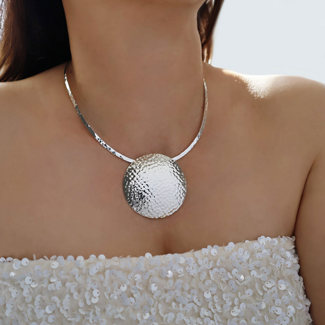 A large statement sterling 925 Silver hammered pendant and choker necklace worn by a woman in a white sequined top.