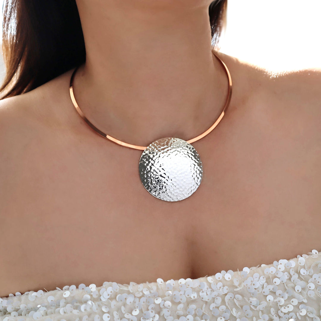A large statement sterling silver pendant on a copper choker necklace worn by a woman with a sparkling evening dress
