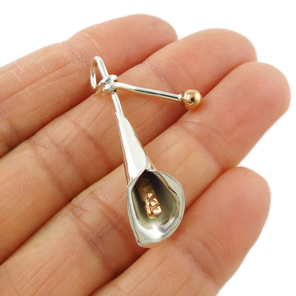 A unique sterling silver and copper mixed metal pendant with a calla lily design, held in a person's hand.