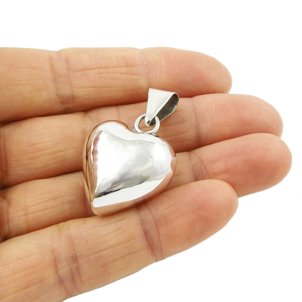 A hand holding a puffed sterling silver pendant necklace with a heart shape.