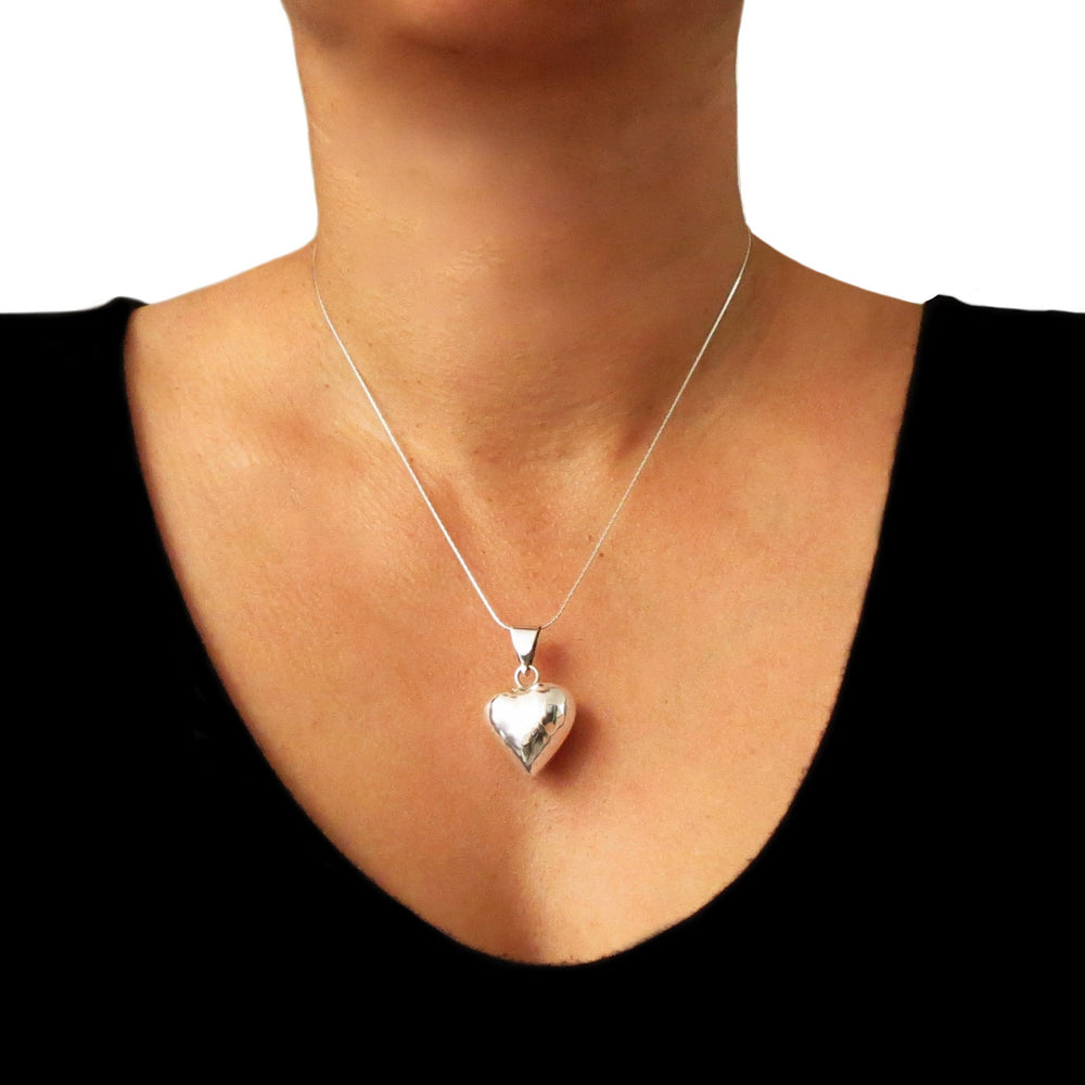 A large hammered sterling silver puffed heart pendant on a chain worn by a woman with a blaxk top. 