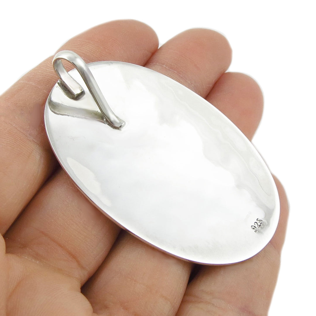 The reverse of a silver pendant held in a hand against a white background
