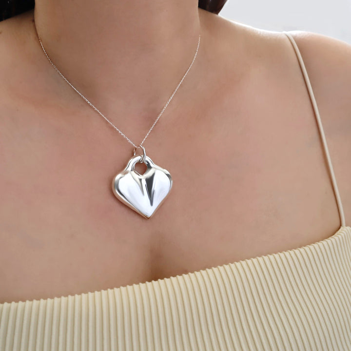 A woman in a yellow top wearing a large silver heart pendant and chain necklace. 