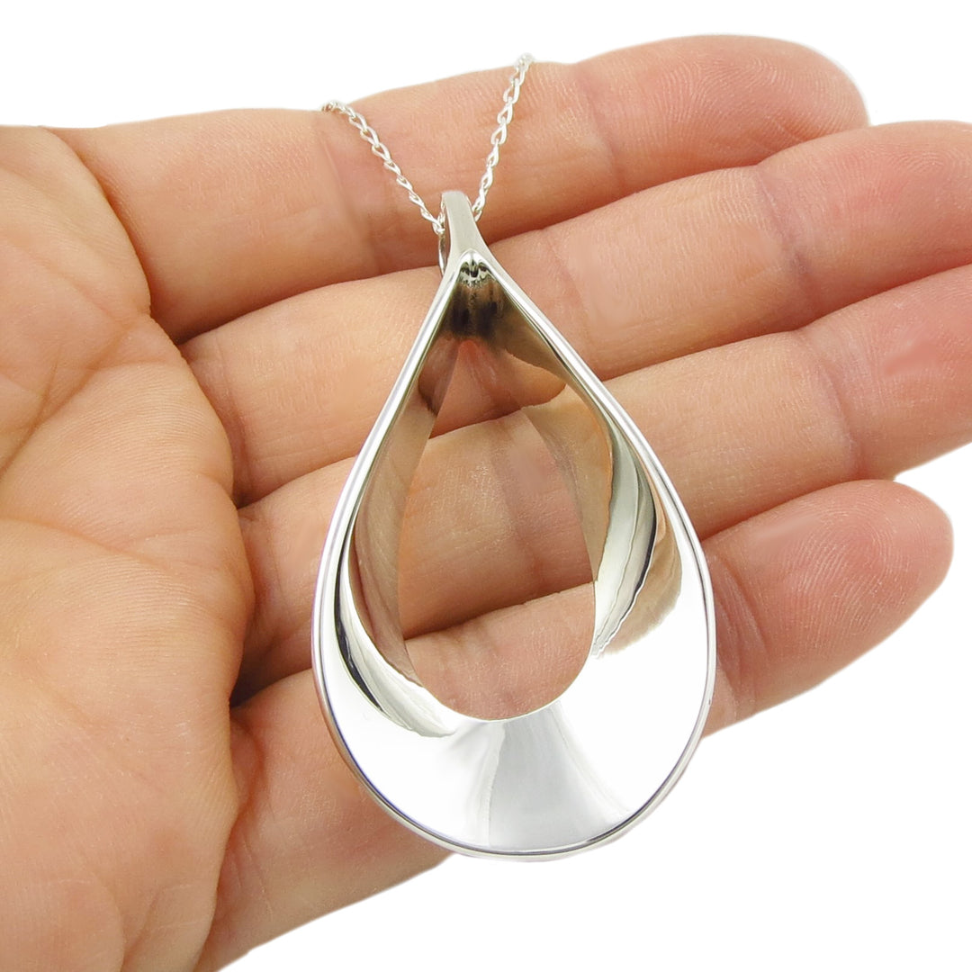 Silver teardrop pendant and chain necklace held in a hand against a white background