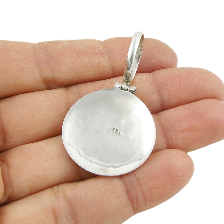 The reverse of a silver pendant with a 25 mark and a large bail held in a person's hand. 