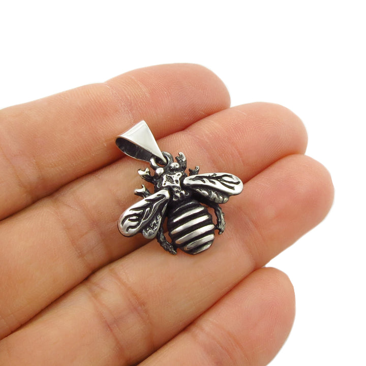 A 925 silver bee pendant with two tone blackened antiqued and polished details, held on a woman's fingers against a plain white background.