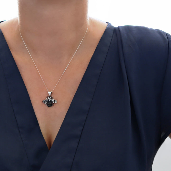 A Mexican sterling 925 silver bee pendant necklace worn by a model in a navy blue V-neck top.