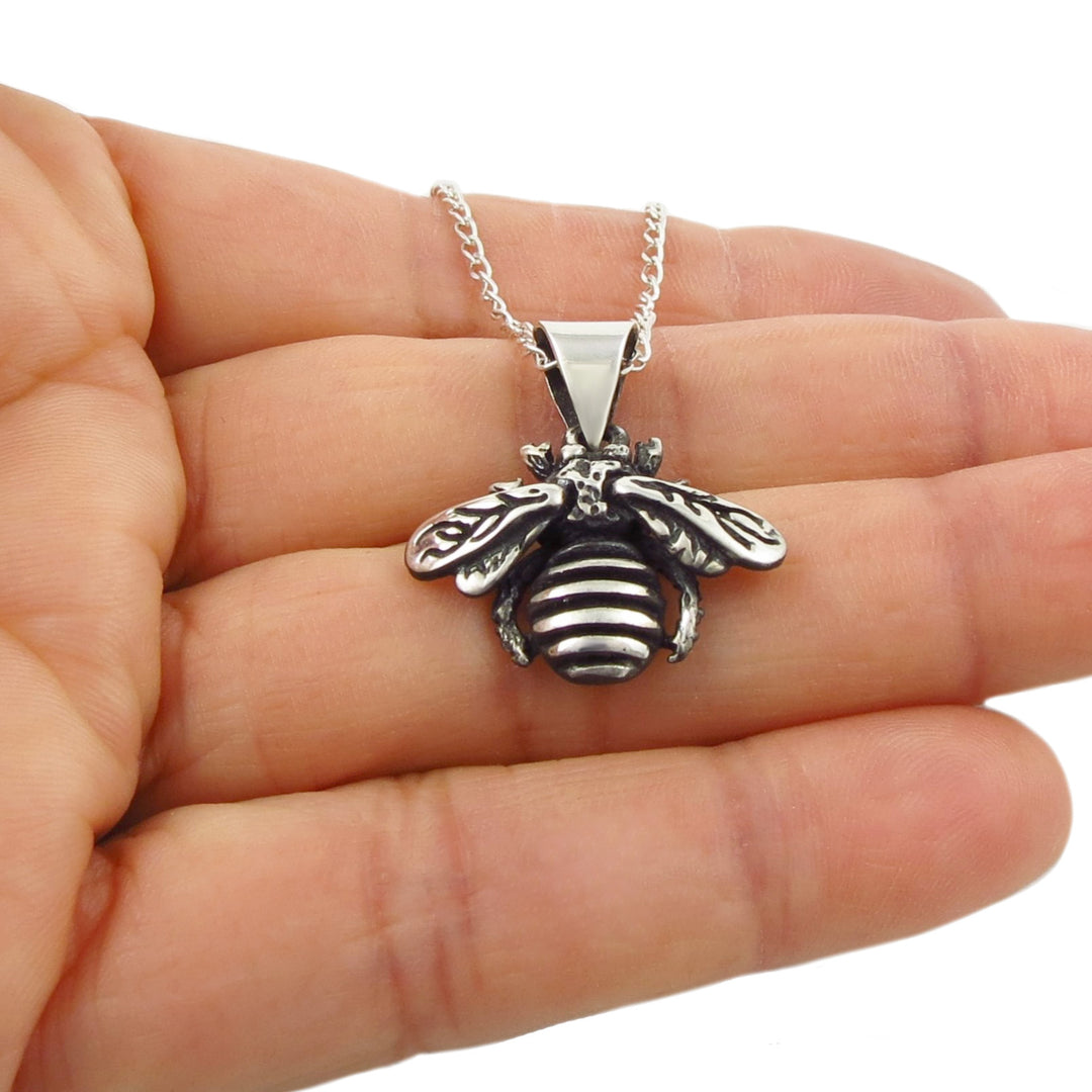 A sterling 925 silver bee pendant and chain necklace held in a person's hand against a plain white background.