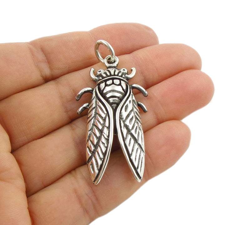 A 925 sterling silver cicada pendant held in a woman's hand against a plain white background.