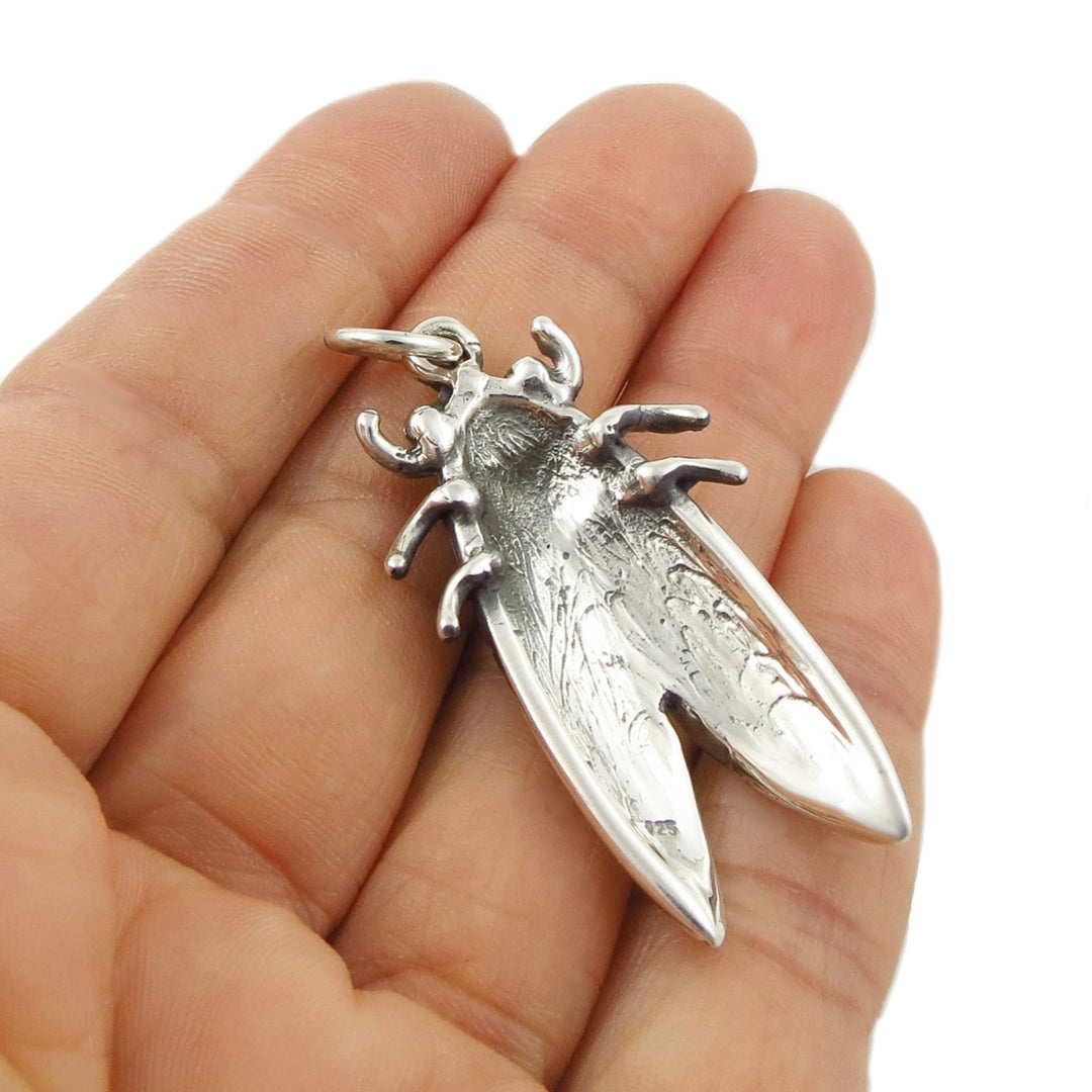 Revere of a 925 sterling silver pendant shaped like a cicada bug insect, resting on a person's hand to show the 925 hallmark against a plain white background.