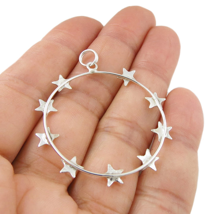 The reverse of a 925 silver circular pendant with star designs held in a hand against a white background
