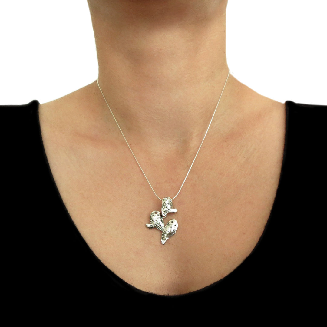 A large prickly pear desert cactus plant pendant and chain in Mexican 925 sterling silver worn by a woman with a dark top. 