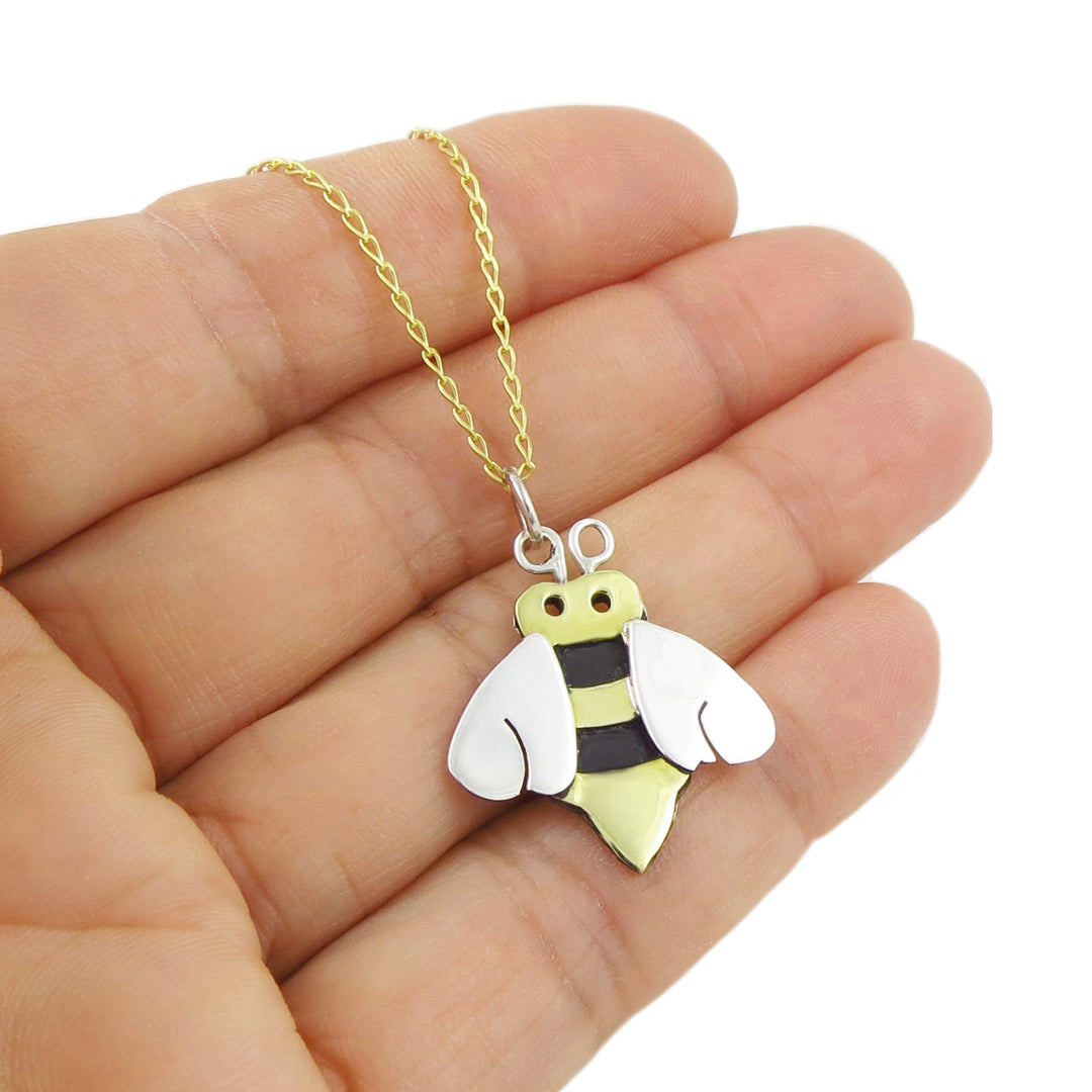 Bee-shaped pendant on a gold chain held in a hand against a white background