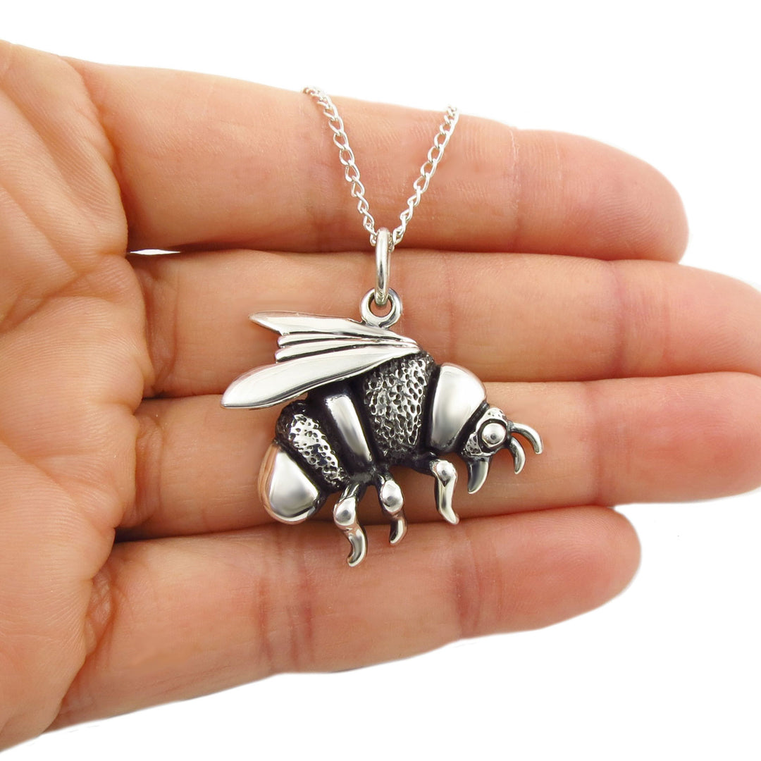 UK hallmarked large sterling 925 silver bee pendant and chain necklace for women held in a hand against a white background