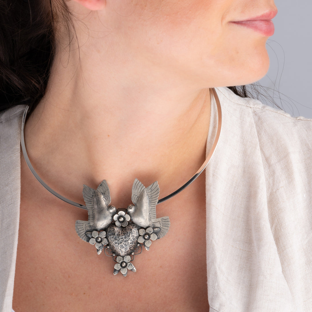 A woman with dark hair wearing a large ornate lovebirds and heart sterling silver pendant and choker necklace 