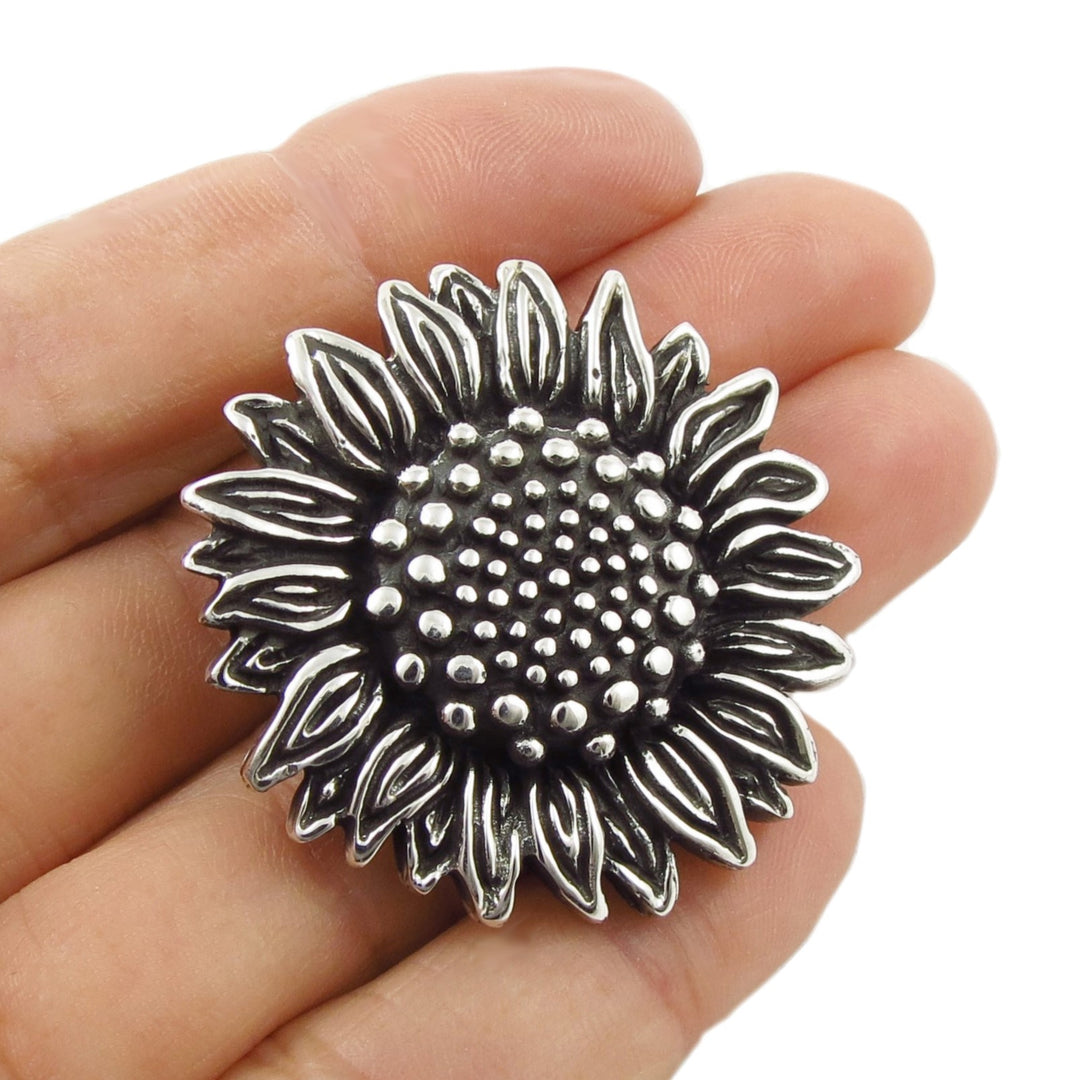 A large sterling 925 silver sunflower-shaped pendant charm held in a person's hand against a plain white background.