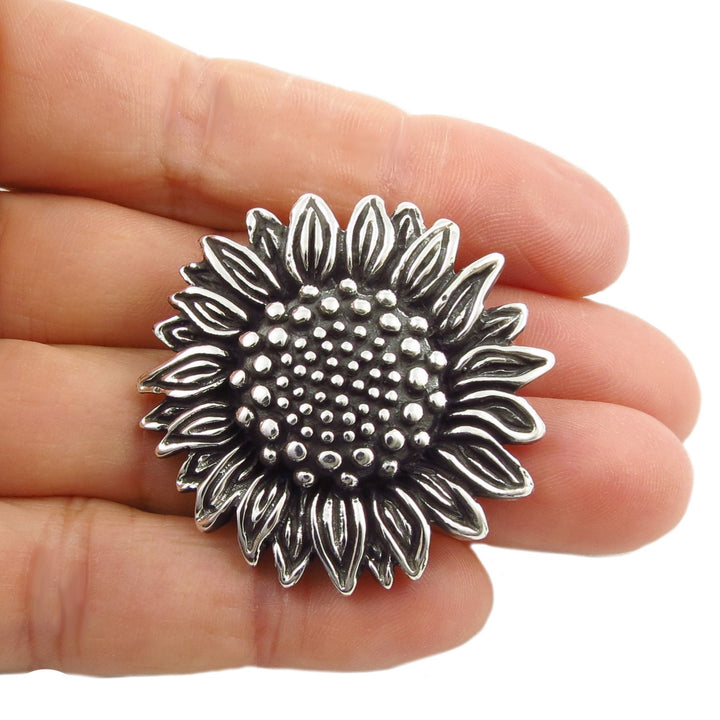 A chunky UK hallmarked sterling 925 silver sunflower-shaped pendant charm  held in a woman's hand on a plain background. 