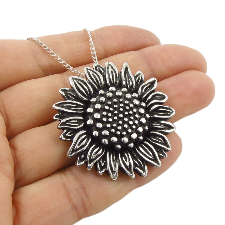 A heavy UK hallmarked sterling 925 silver sunflower pendant and chain necklace held in a person's hand against a plain white background.