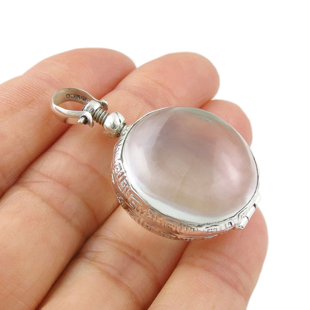 Sterling silver locket pendant with clear glass held in a person's hand. 