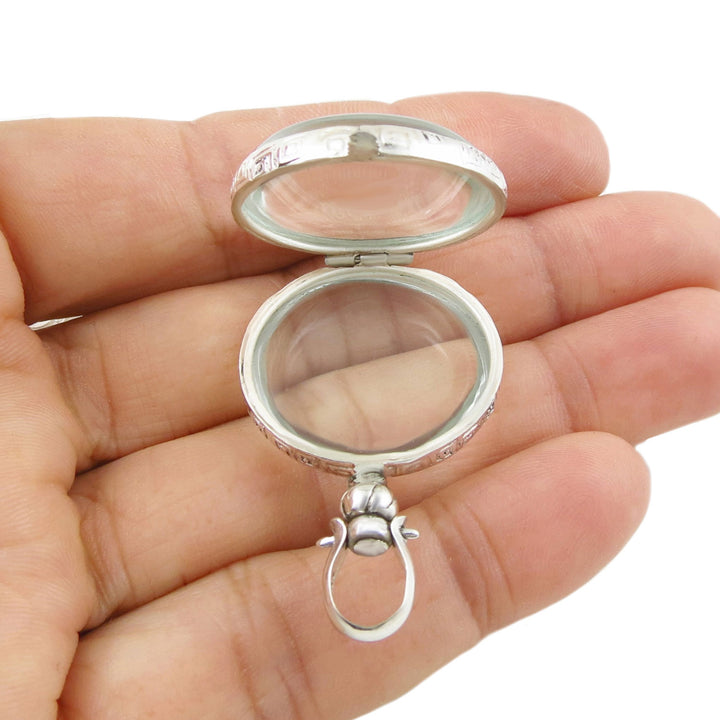 A large sterling 925 silver locket pendant withclear glass held in a person's hand. 