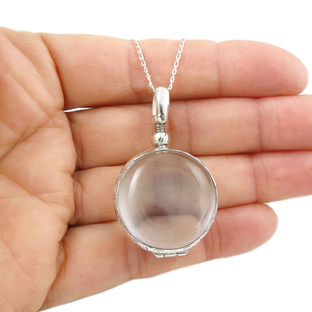Sterling silver locket pendant with clear glas hanging on a chain held in a person's hand. 
