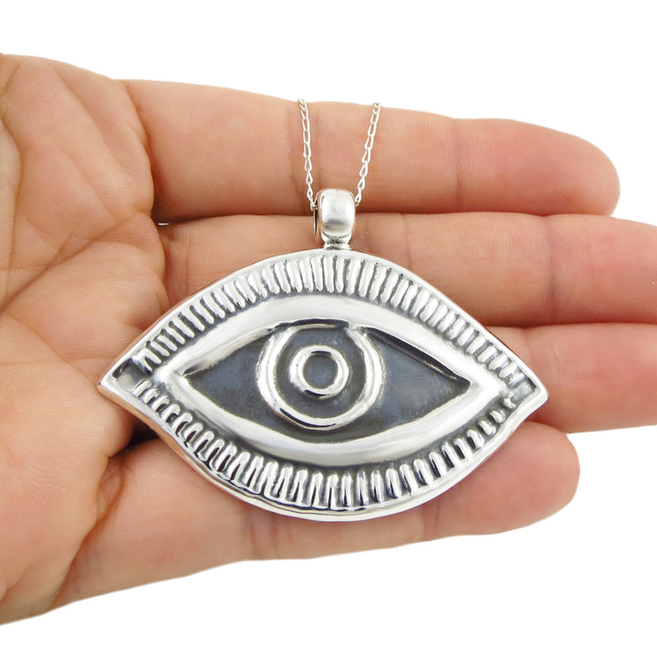 A large evil eye lucky 925 sterling silver pendant and chain necklace showcased in a woman's hand on a white background. 